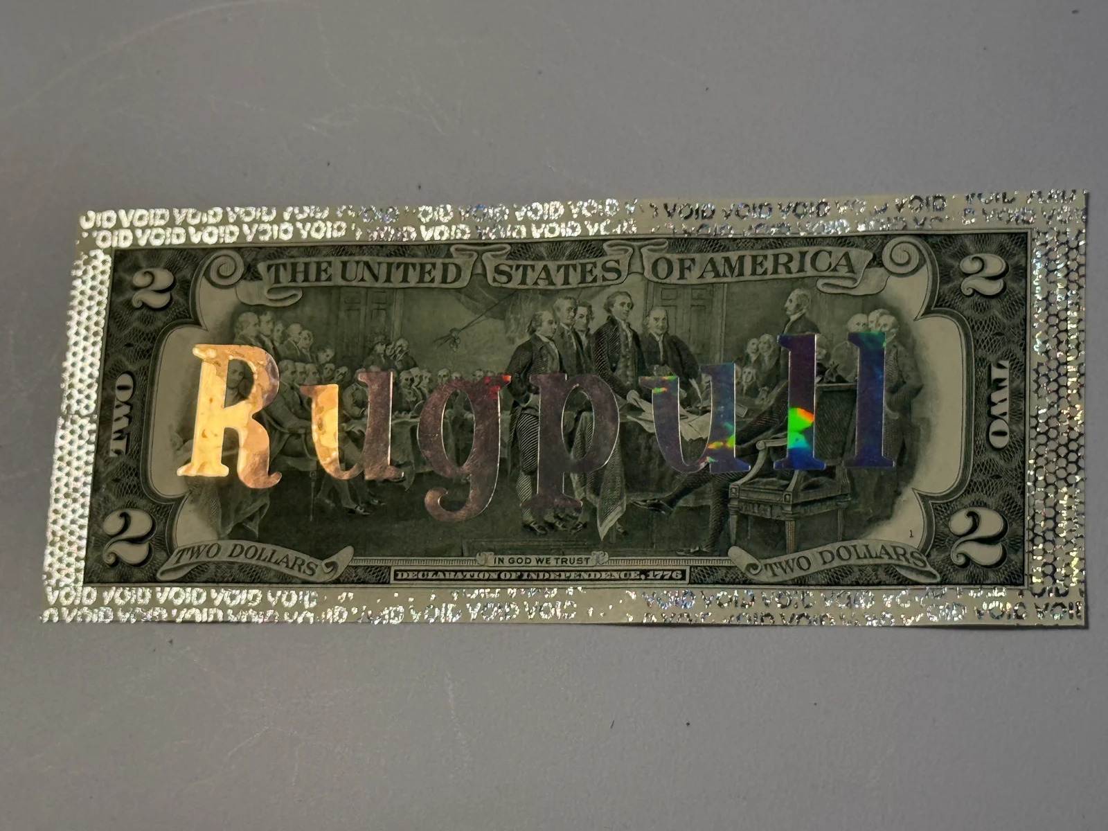 Rugpull photographed in shifting light, with reflective letters on a real $2 bill.